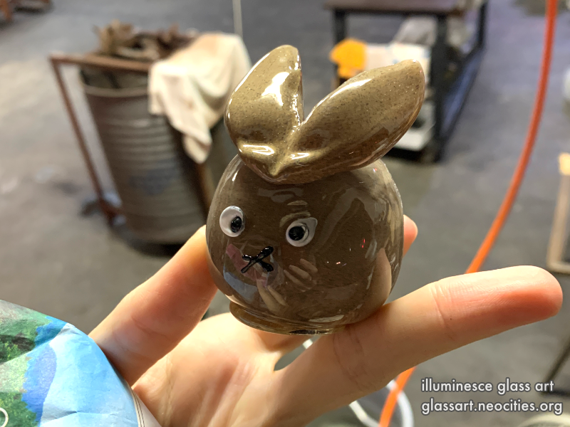 A hand holding a brown, glass rabbit in a glass shop.