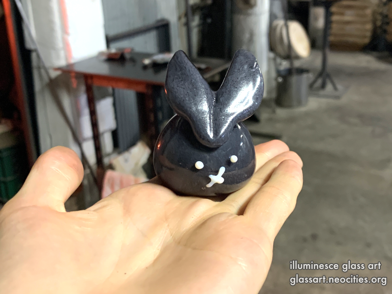 A hand holding a black, glass rabbit in a glass shop.