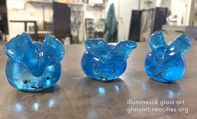 A front view of three bright blue, round rabbits.